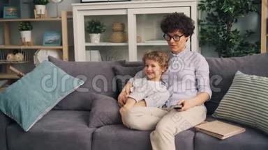 母亲和儿子一起坐在沙发上，在家看电视聊天，微笑